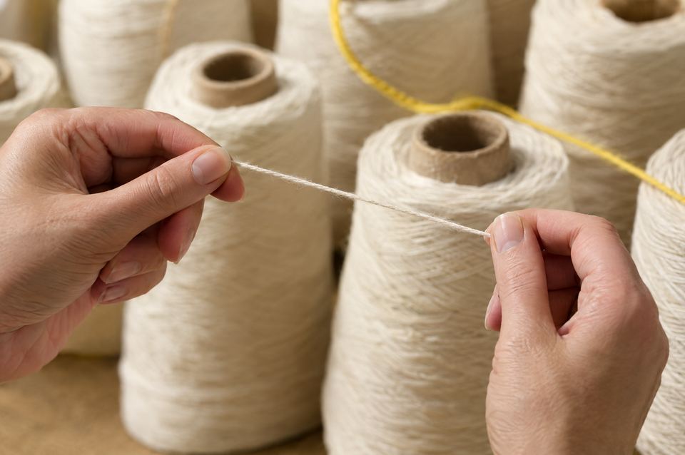Hands checking a thread in front of a row of yarn cones